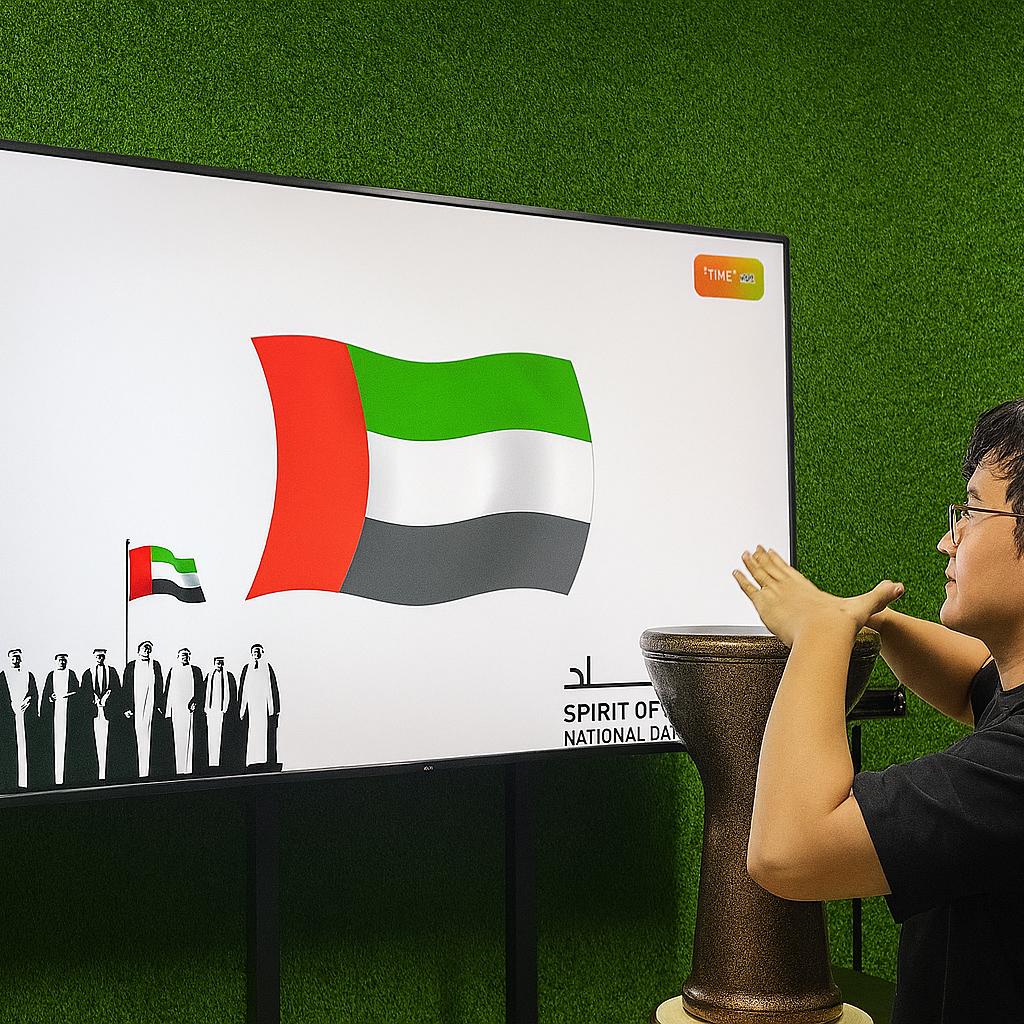 Guest playing Drum-to-Reveal interactive game at a Dubai event, beating the drum to reveal a hidden image on a large screen, designed for exhibitions and activations.